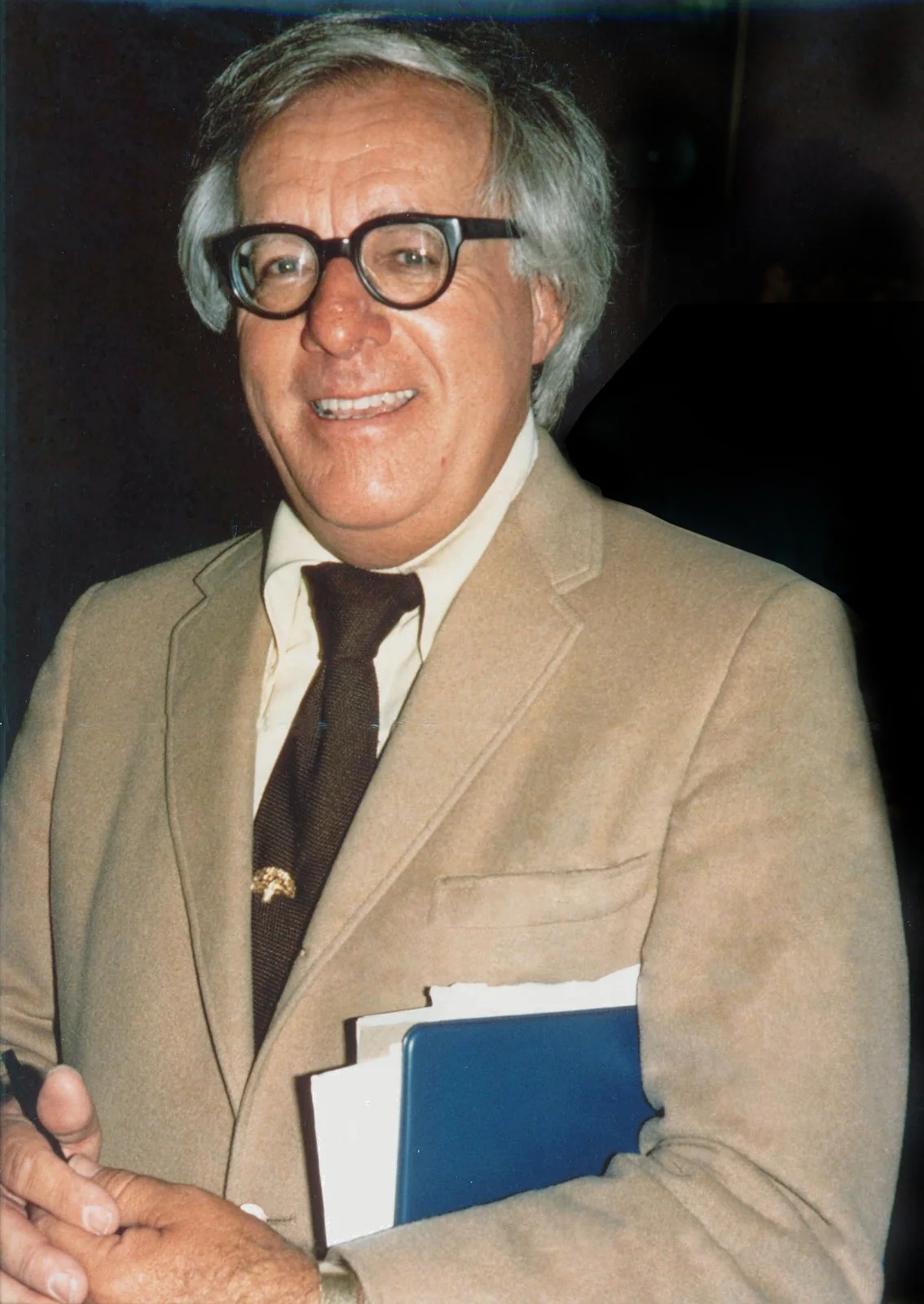 Ray Bradbury souriant, lunettes noires et veste claire, un livre sous le bras
