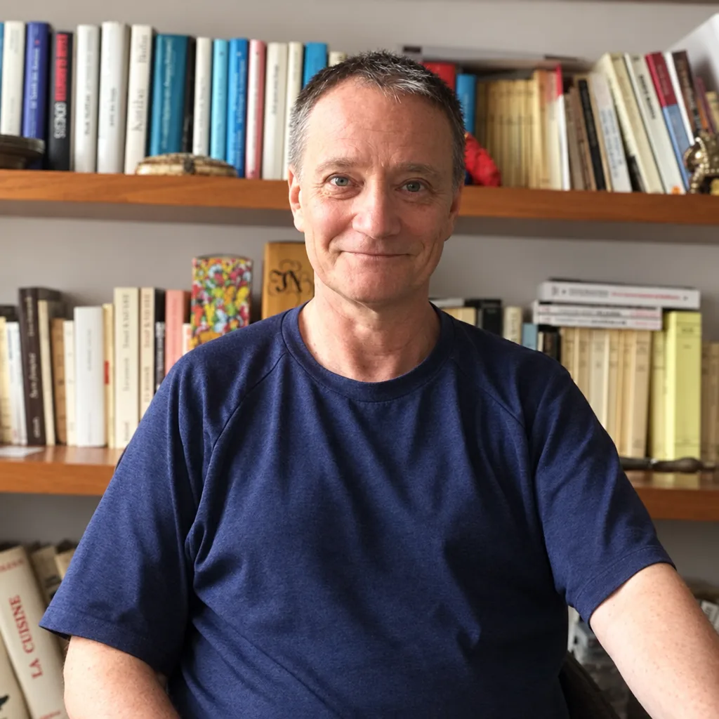 Pierre-François Bertrand, souriant, devant sa bibliothèque